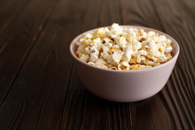 Bowl with popcorn on dark wooden table with copyspace