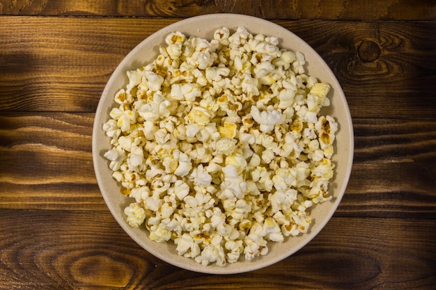 Bowl with popcorn on wooden table. Top view