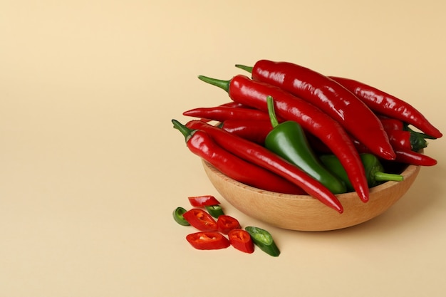 Bowl with red and green hot peppers on beige background