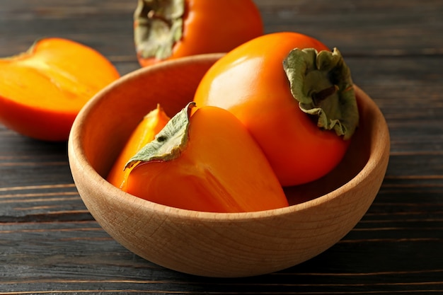 Bowl with ripe persimmon on wooden background