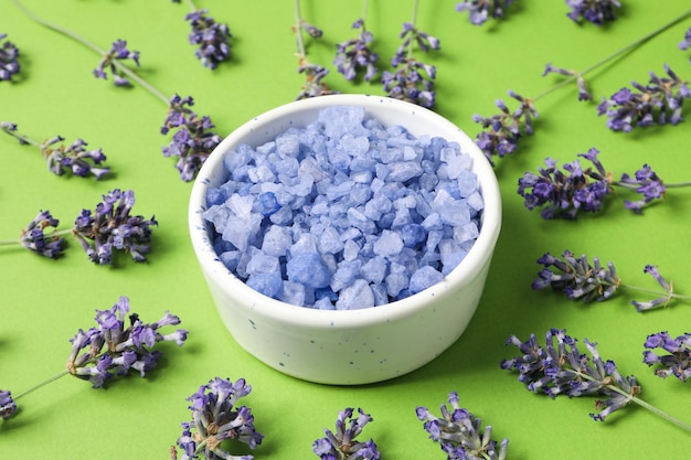 Bowl with salt and lavender flowers on green background