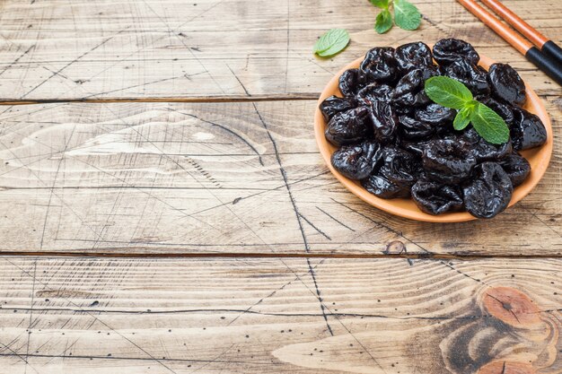 Bowl with tasty dried plums on wooden table Copy space