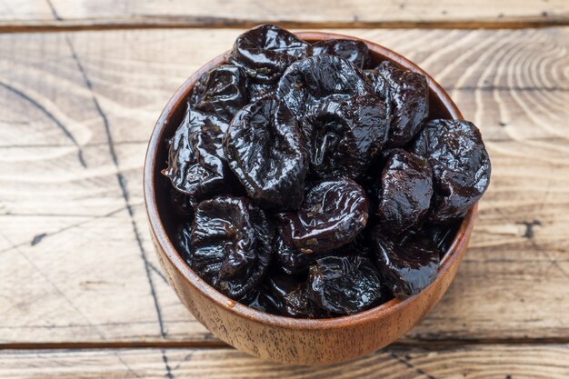 Bowl with tasty dried plums on wooden table