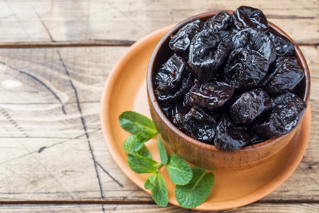 Bowl with tasty dried plums on wooden table 