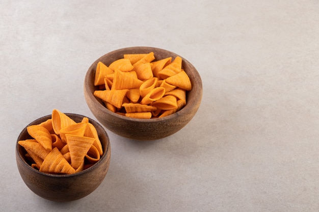 Bowls of chips, crackers and sunflower seeds on stone surface.