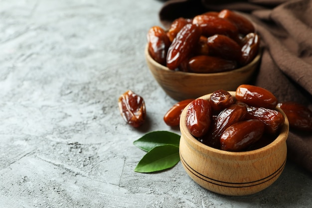 Bowls of dried dates and kitchen napkin on gray textured background