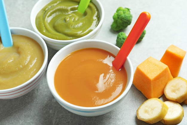 Bowls with baby food on grey background