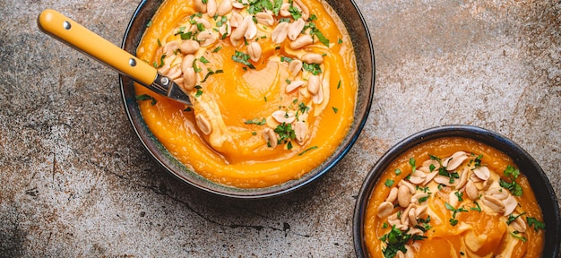 Bowls with pumpkin cream soup with peanuts on rustic metal background