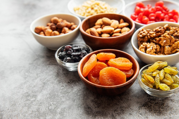 Bowls with various dried fruits and nuts on a gray concrete surface