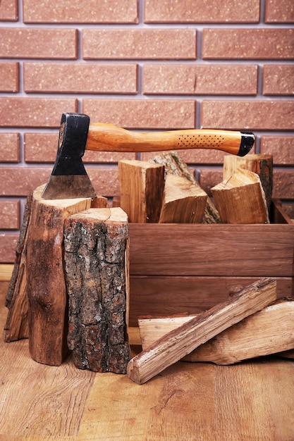 Box of firewood and axe on floor on brick background