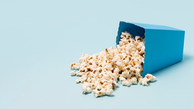 Box of popcorn spilled on blue background