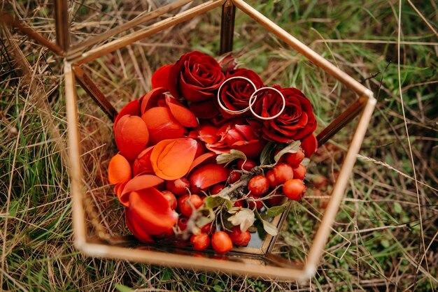 A box of red roses and a pair of wedding rings sits on the grass.