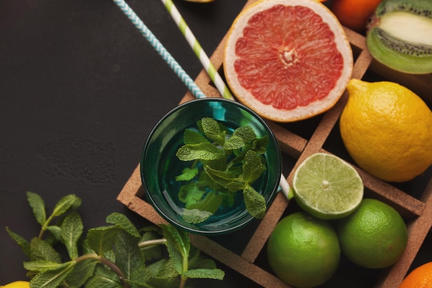 Box with assortment of citruses on gray background, closeup. Gasses with juice, oranges, lemons, tangerines and other exotic fruits, flat lay. Making detox freshes concept