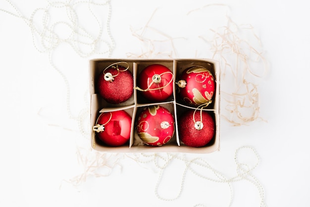 Box with bright red christmas balls on white background.