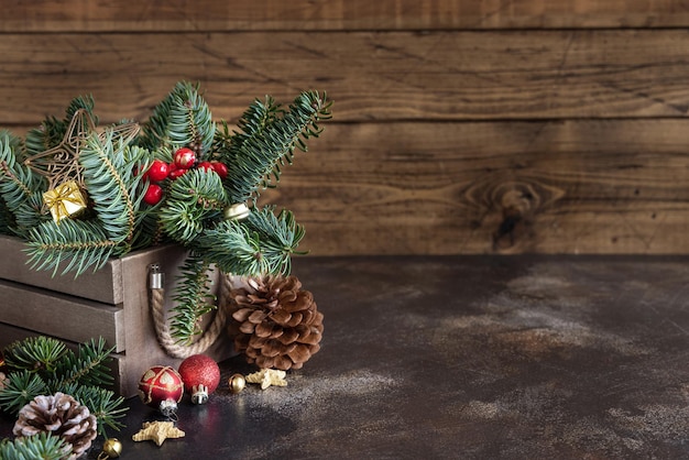 Box with Christmas decorations pine cones and green fir branches close up on wooden table