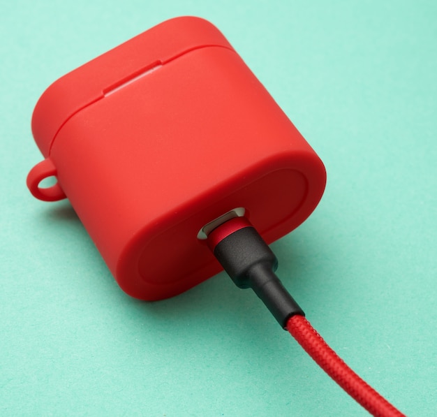 Box with a headphone charger in a red case attached to the cable on a green background