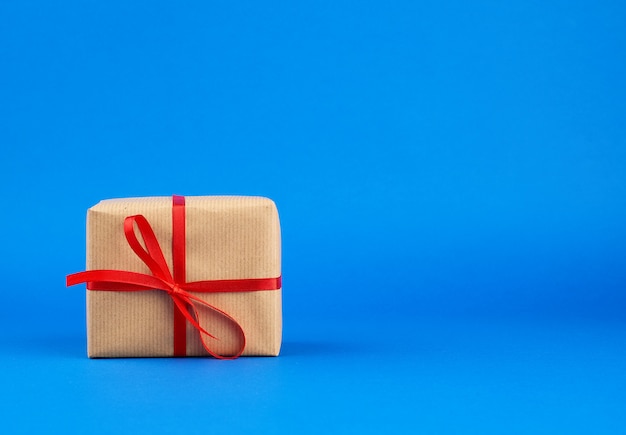 Box wrapped in brown paper and tied with a red bow, gift on blue