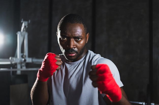 Boxer in gym aggressive african man fighter resting after training boxing ready for fight looking at