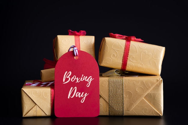 Photo boxing day sale text on a red tag with stack of gift boxes on black background. online sho