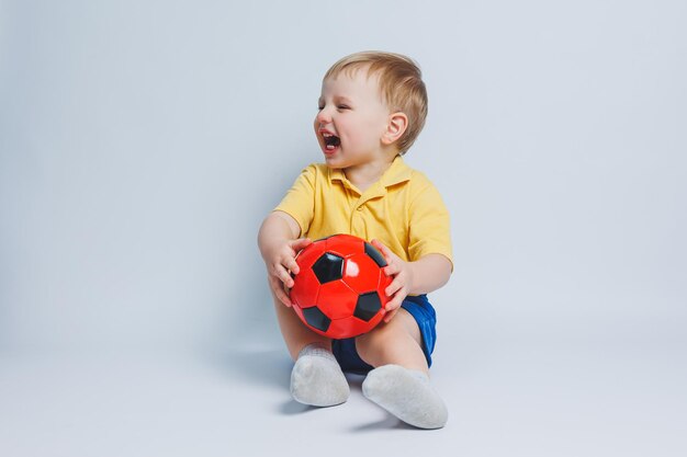 Boy 34 years old football fan in a yellow Tshirt with a ball in his hands holding a soccer ball in his hands isolated on a white background The concept of sports family recreation