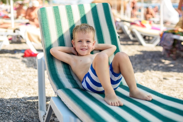 a boy of 4 years old in striped shorts lies on a sunbed on the beach contented and happy Summer