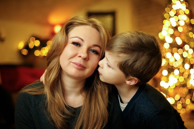 Boy 5-7 years old kisses his mother in a festive New Year's interior