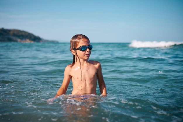 Boy of 8 years old swims in the sea in blue swimming goggles in the evening