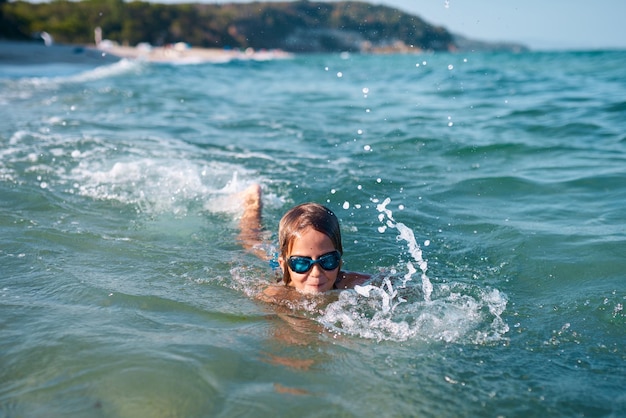 Boy of 8 years old swims in the sea in blue swimming goggles in the evening