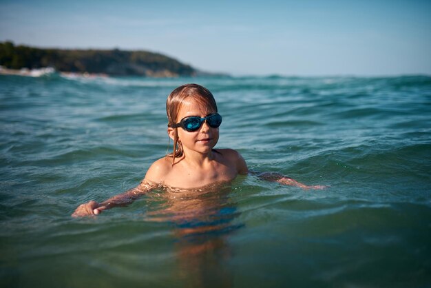 Boy of 8 years old swims in the sea in blue swimming goggles in the evening