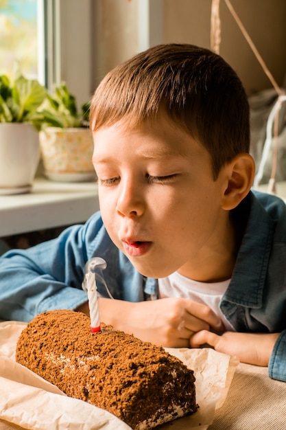 Boy of 9 years old blows out the candle on the cake. celebrating birthday at home. Home holiday for children. portrait of a boy blowing on a candle. Make a wish. Fulfillment of desires