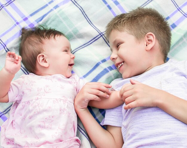 Photo the boy and the baby lie on the bedspread smiling and looking into each other's eyes