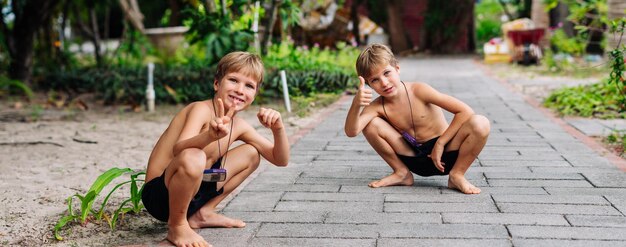 Boy blond freckles squatting sit smiling show gesture thumbs up shirtless bare chested shorts nature