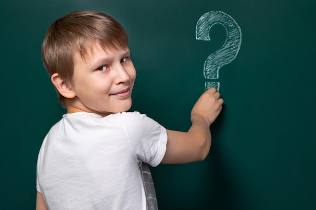 A boy of Caucasian appearance writes a question mark on the chalkboard.  Smile. Easy solution to the problem.