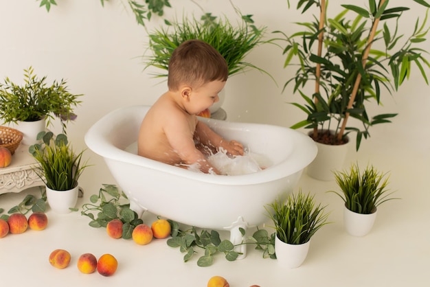 A boy child is sitting in the bathroom with milk on a white background with peaches and rejoices.