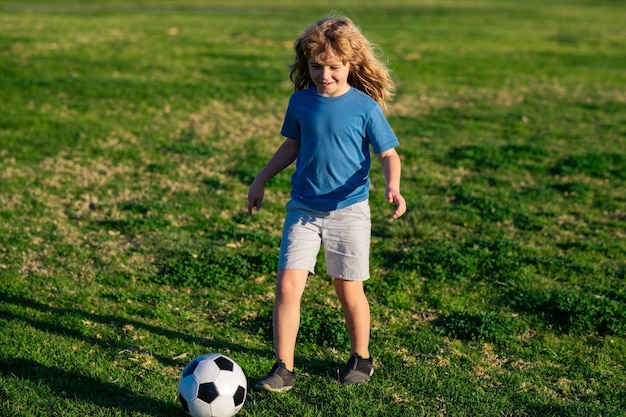 Boy child playing football on football field kid playing soccer kid kicking a football ball on a grass