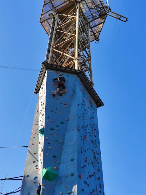 A boy climbs a high tower with walls for climbing on hooks in special equipment View from below