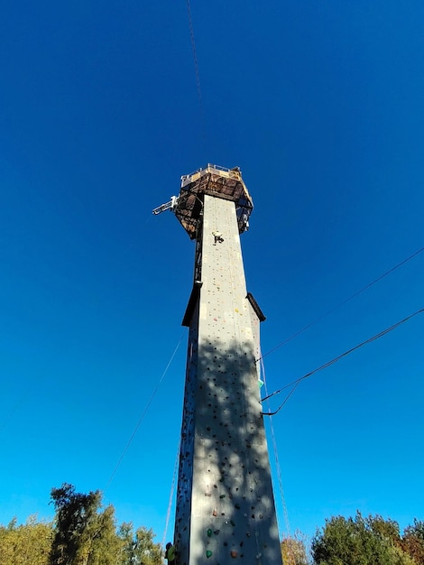 A boy climbs a high tower with walls for climbing on hooks in special equipment View from below