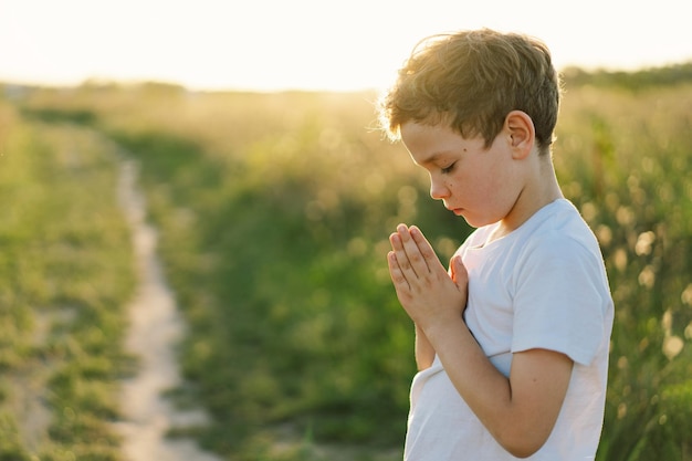 Boy closed her eyes and praying in a field at sunset Hands folded in prayer concept for faith spirituality and religion