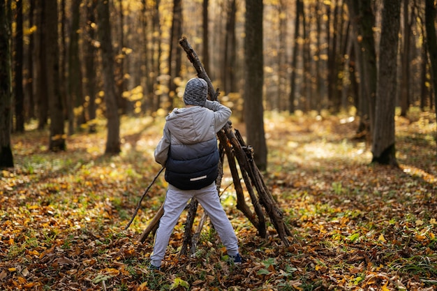 Boy constructs a house from sticks in autumn forest