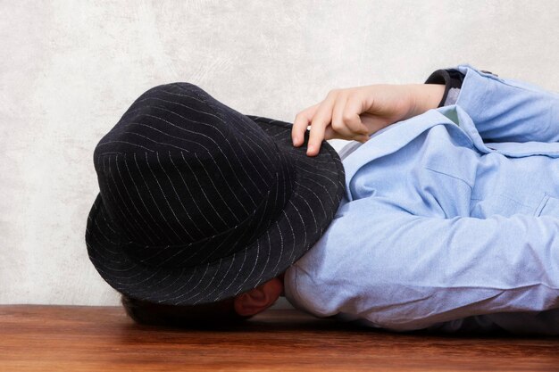 The boy covered his face with a hat and lies on the table Hiding