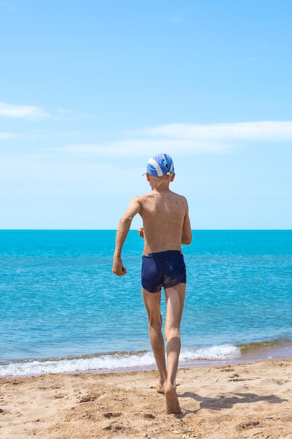 A boy covered in sand runs to plunge into the sea Merry summer holidays