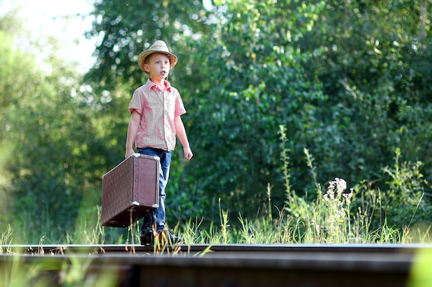 Boy cowboy with suitcase waiting a train and railroad western travel concept