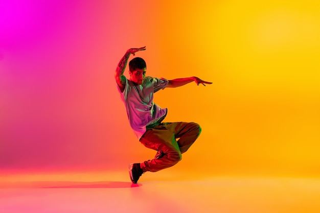 Boy dancing hip-hop in stylish clothes on gradient background at dance hall in neon light.