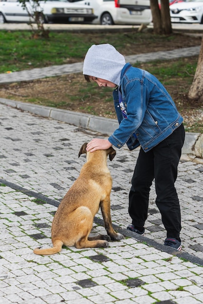 Boy in a denim jacket petting a street dog