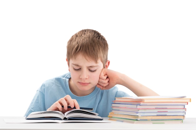 Boy doing homework at table and attentively reads book Portrait of schoolboy at desk with stack of notebooks is isolated on white background