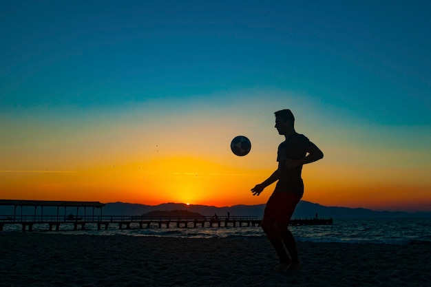 Boy doing sports with ball on the beach in full summer sunset on the Brazilian coast