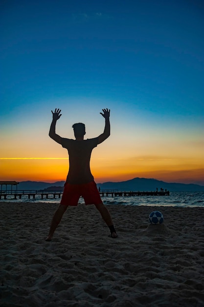 Boy doing sports with ball on the beach in full summer sunset on the Brazilian coast