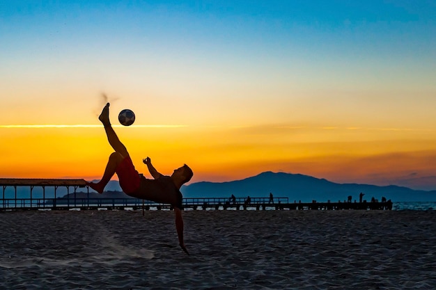 Boy doing sports with ball on the beach in full summer sunset on the Brazilian coast