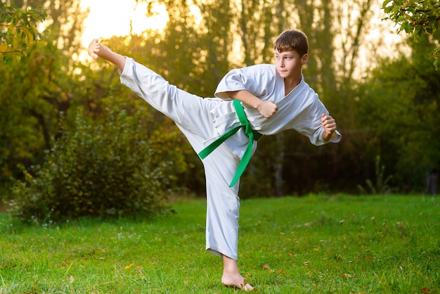 Boy dressed kimono doing karate exercises outdoors