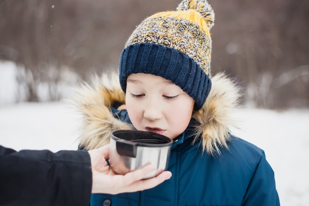 A boy drinks from a thermos of tea or a drink , winter walking, Hiking, winter, winter clothing